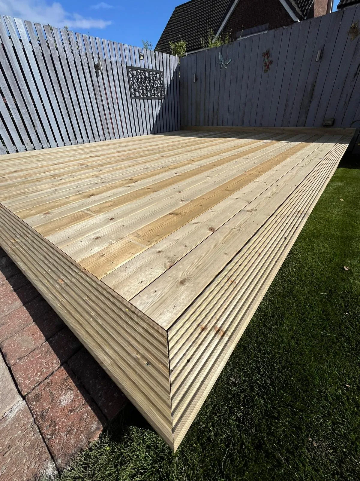 A wooden deck in a backyard next to a fence.